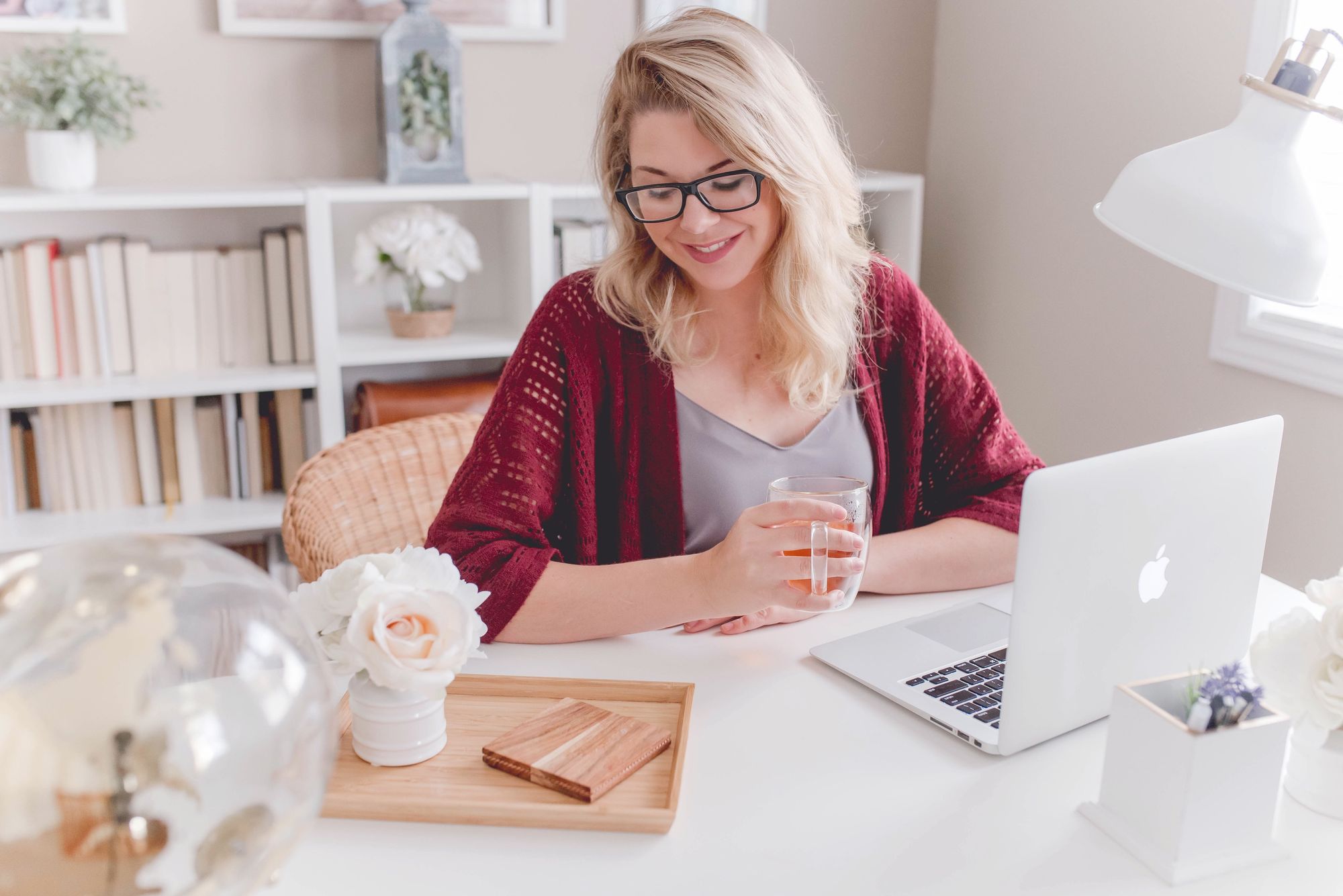 Femme tenant une tasse de thé devant un ordinateur portable dans un bureau à domicile.
