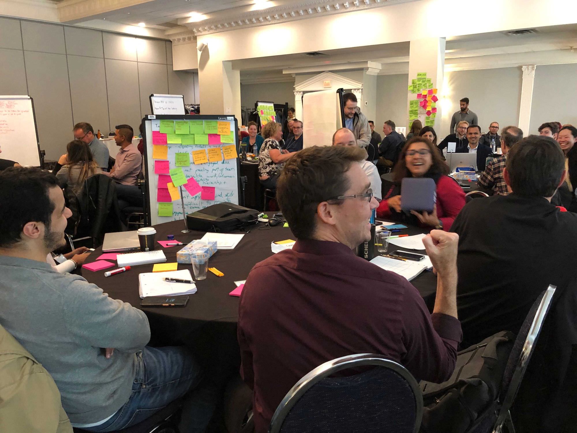 Large groups of people seated at tables enthusiastically participating in team activities. 